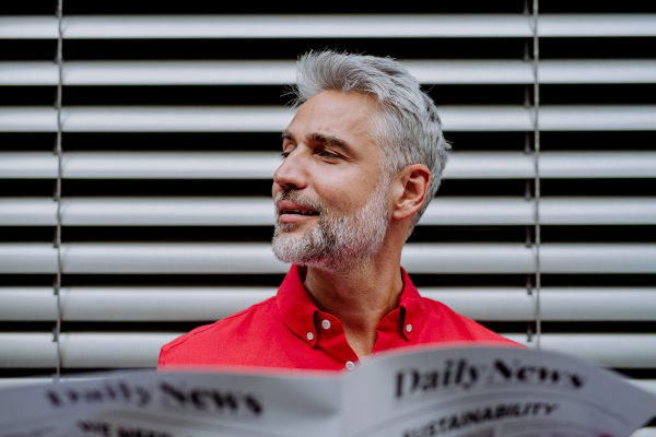 A mature businessman sitting at balocny and reading newspaper.