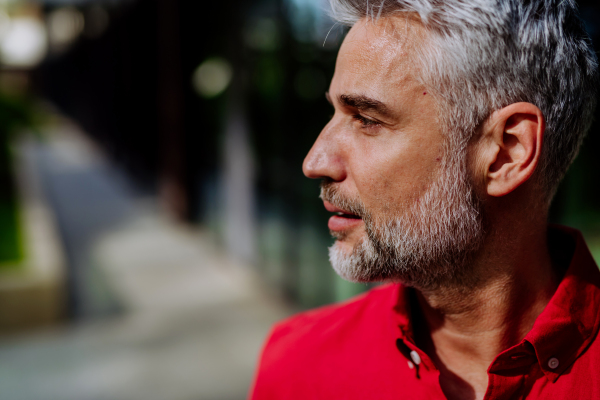 Portrait, side view of mature businessman in red shirt standing on the street.