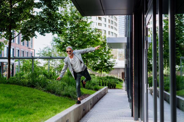 A fun portrait of happy energetic mature businessman with arms outstretched balancing on wall , feeling free, work life balance concept.