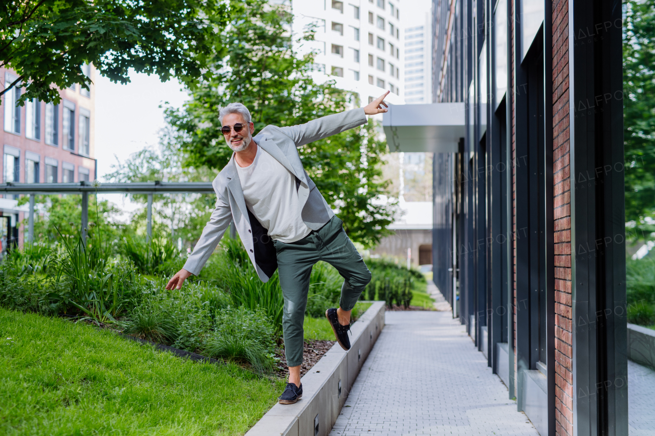 A fun portrait of happy energetic mature businessman with arms outstretched balancing on wall , feeling free, work life balance concept.