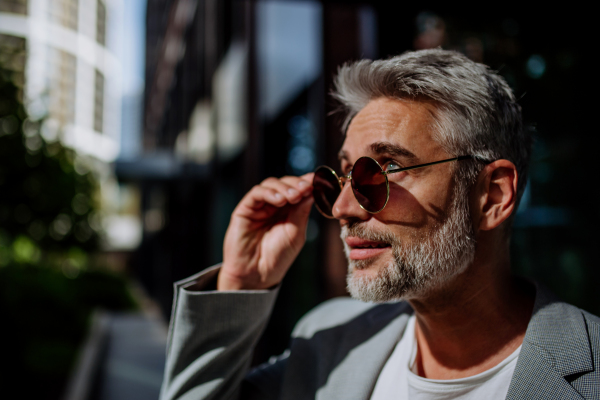 Portrait, side view of mature businessman in suinglasses standing on the street.