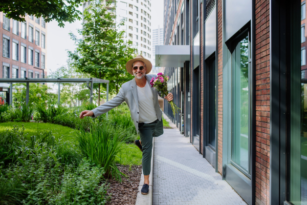 A portrait of happy energetic mature man with flower bouquet balancing on wall , feeling free, life balance concept.