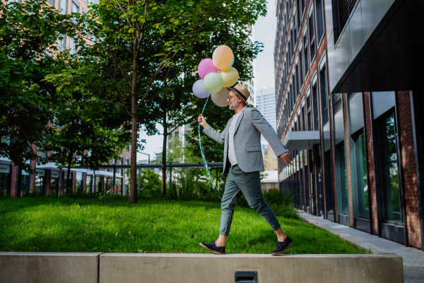 A fun portrait of happy energetic mature businessman holding balloons and walking on wall , feeling free, work life balance concept.