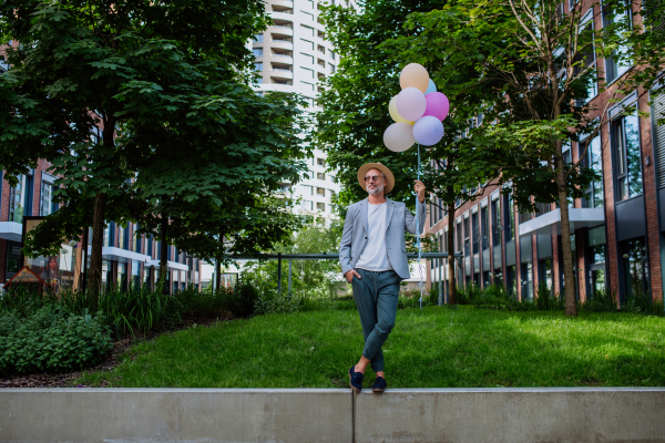 A fun portrait of happy energetic mature businessman holding balloons and walking on wall , feeling free, work life balance concept.