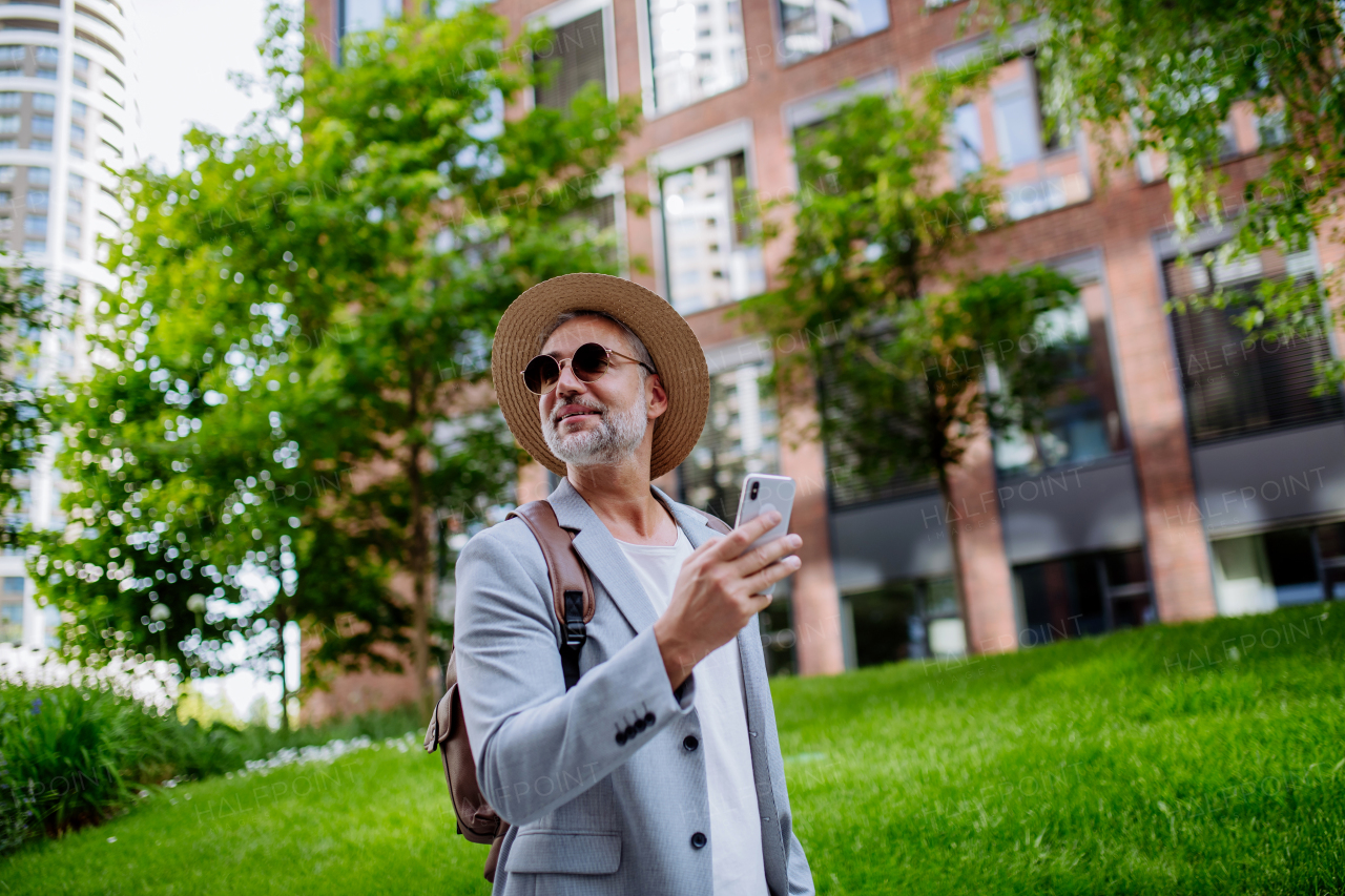 A confident man wearing straw hat and backpack,using phone, businessman in casual clothes in summer on the way to work.