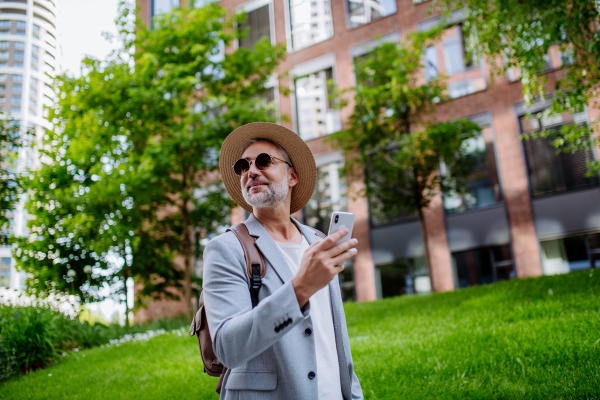 A confident man wearing straw hat and backpack,using phone, businessman in casual clothes in summer on the way to work.