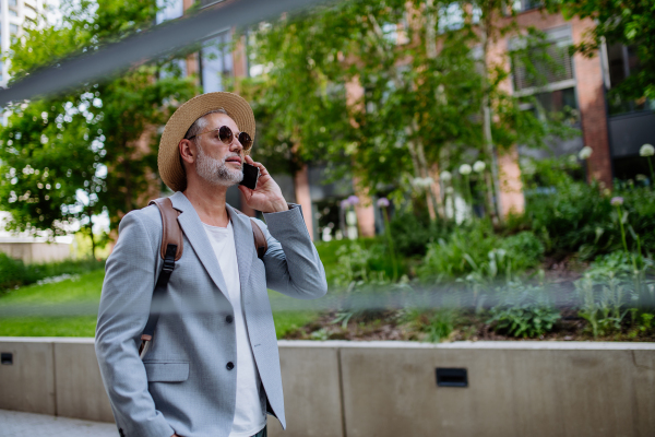 A confident man wearing straw hat and backpack talking on phone, businessman in casual clothes in summer on the way to work.