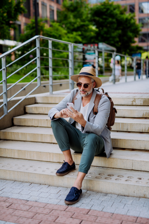 A confident man wearing straw hat and backpack,using phone, businessman in casual clothes in summer on the way to work.