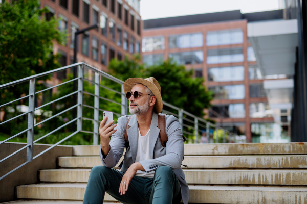 A confident man wearing straw hat and backpack,using phone, businessman in casual clothes in summer on the way to work.