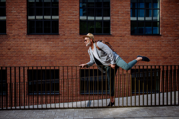 A fun portrait of happy energetic mature businessman wearing straw hat and backpack climbing over the fence , feeling free, work life balance concept.