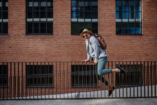 A fun portrait of happy energetic mature businessman wearing straw hat and backpack climbing over the fence , feeling free, work life balance concept.