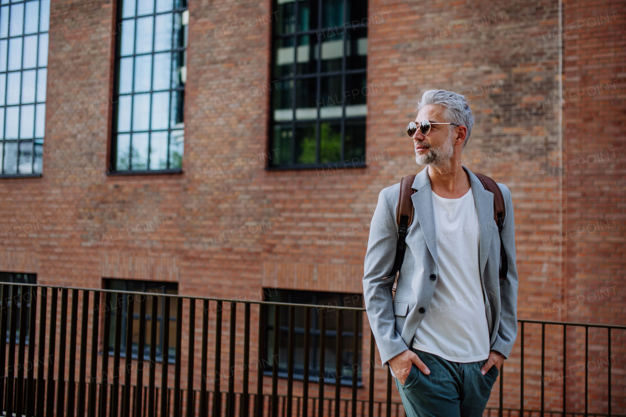 A confident man wearing backpack walking in street, businessman in casual clothes in summer on the way to work.