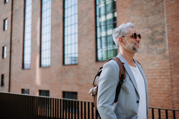 A confident man wearing backpack walking in street, businessman in casual clothes in summer on the way to work.