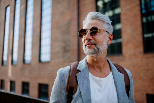 A confident man wearing backpack walking in street, businessman in casual clothes in summer on the way to work.