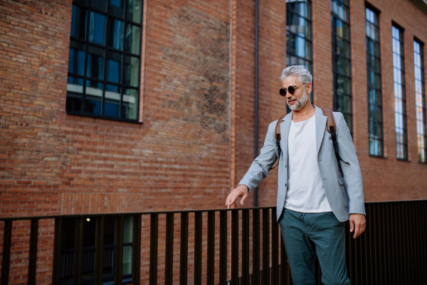 A confident man wearing backpack walking in street, businessman in casual clothes in summer on the way to work.