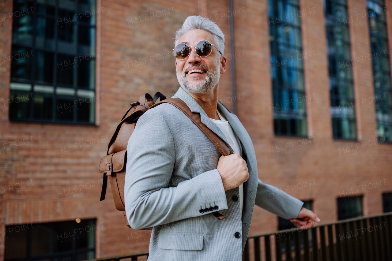 A confident man wearing backpack walking in street, businessman in casual clothes in summer on the way to work.