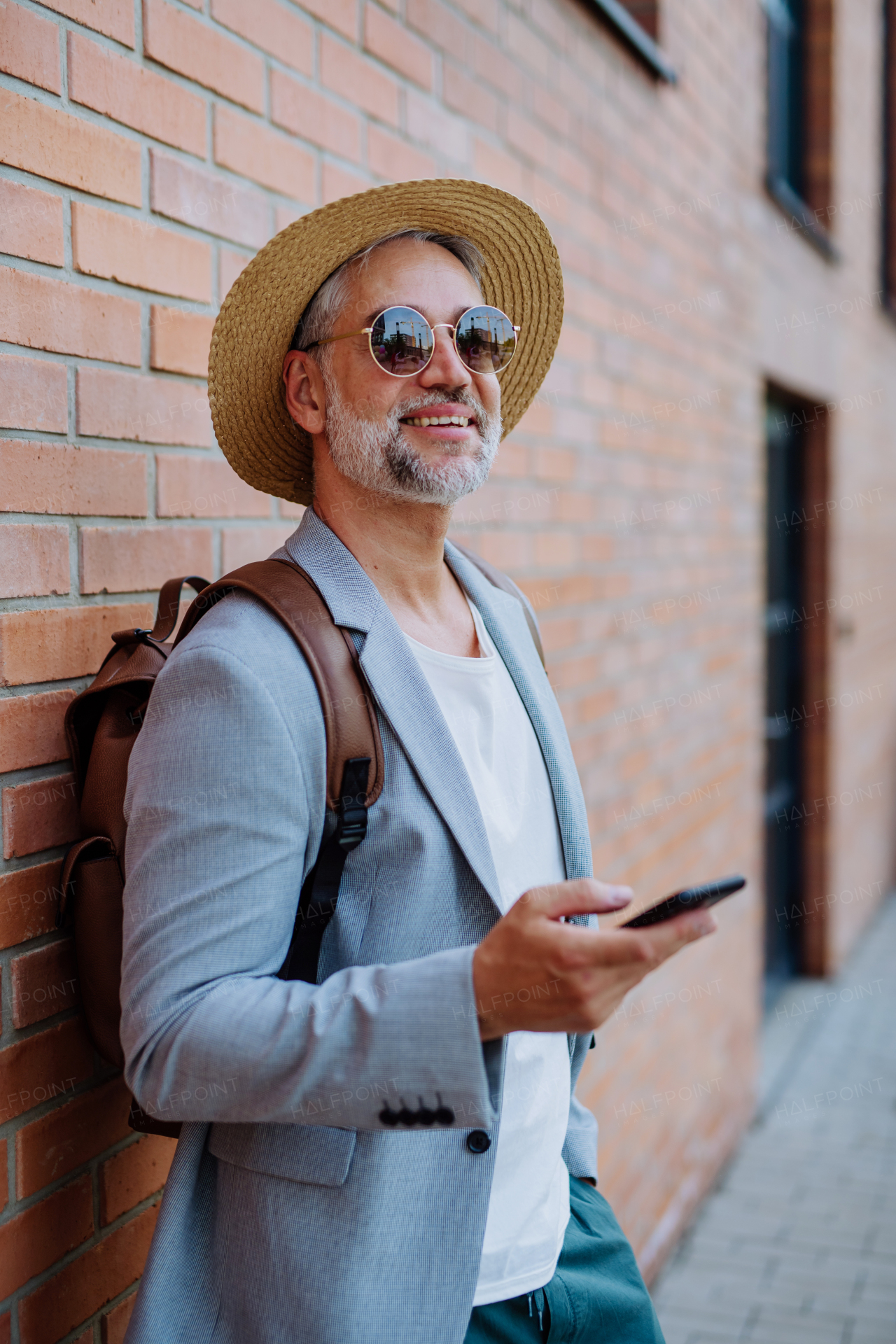 A portrait of confident man wearing straw hat and backpack using smartphone, businessman in casual clothes in summer on the way to work.