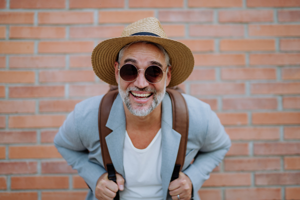 A portrait of confident man wearing straw hat and backpack looking at camera, businessman in casual clothes in summer on the way to work.