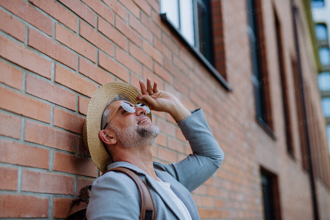 A portrait of confident man wearing straw hat and backpack, businessman in casual clothes in summer on the way to work.