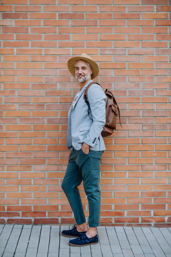 A portrait of confident man wearing straw hat and backpack looking at camera, businessman in casual clothes in summer on the way to work.