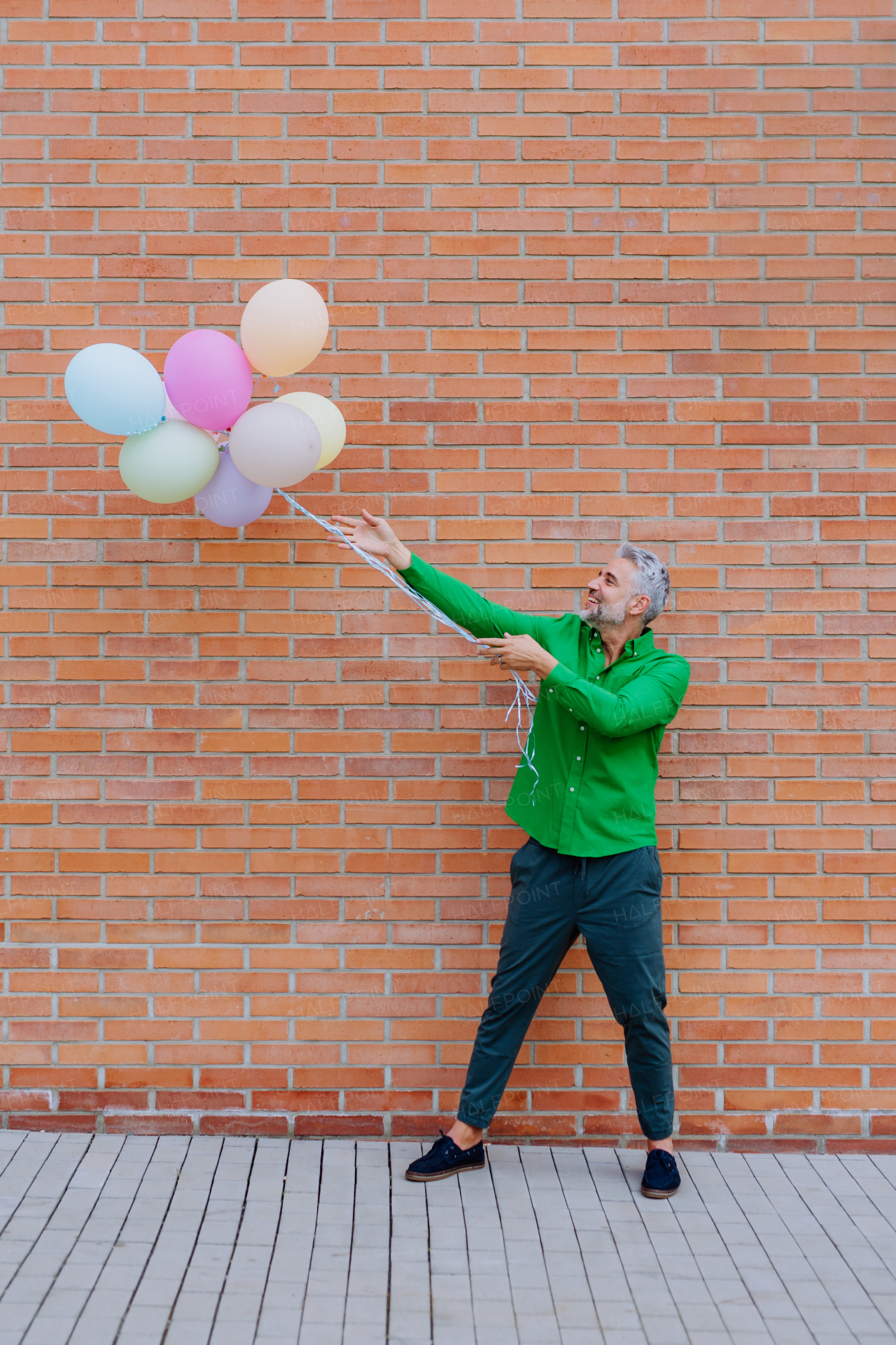 A fun portrait of happy energetic mature businessman holding balloons in street, feeling free, work life balance concept.