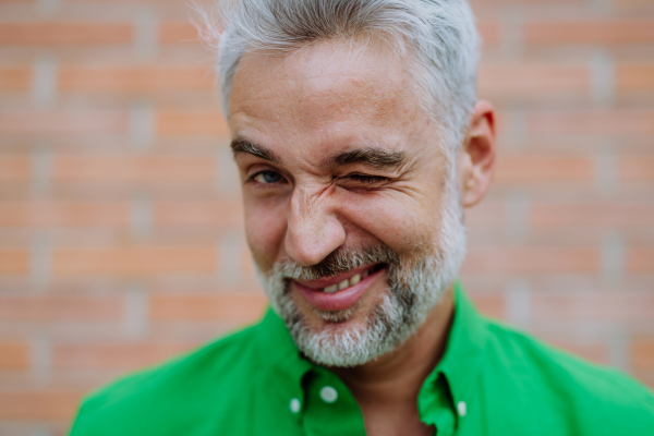 A mature businessman with winking and making funny grimace on street background.