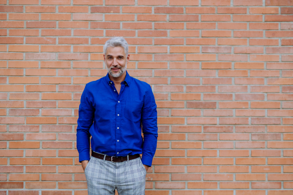 Portrait of a confident man wearing business clothes looking at camera, standing in front of brick wall.