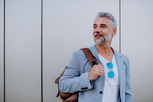 A confident man wearing backpack walking in street, businessman in casual clothes in summer on the way to work.