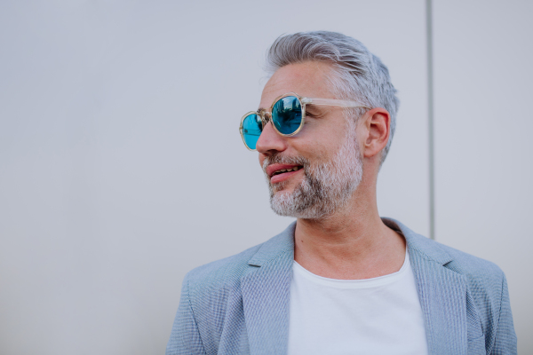 A portrait of uccessful happy businesswoman wearing causal clothes and sunglasses in summer in street looking away.