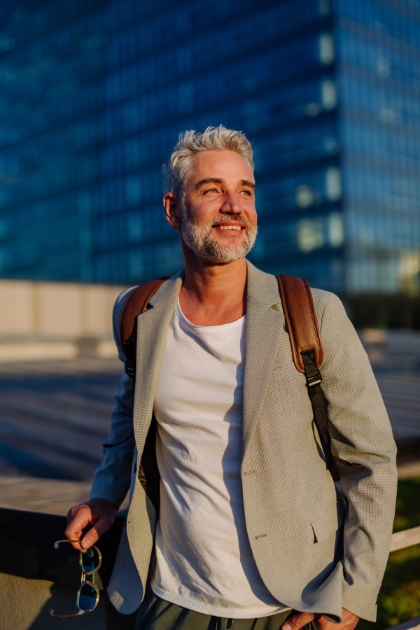 A portrait of happy energetic mature businessman in city, feeling free, work life balance concept.