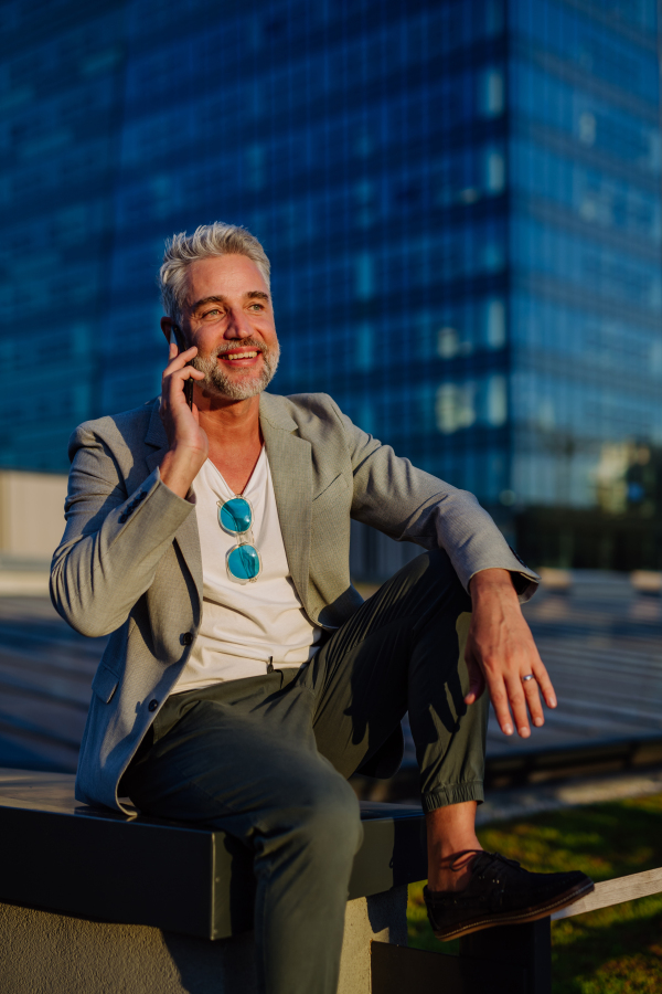 A confident businessman with backpack sitting on stairs and using phone, feeling free, escaping from work, work life balance concept.