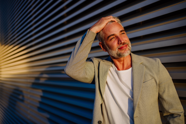 A mature relaxed businessman leaning on street wall during sunset, work life balance concept.