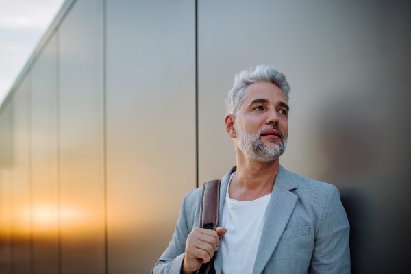 A mature relaxed businessman leaning on street wall, work life balance concept.