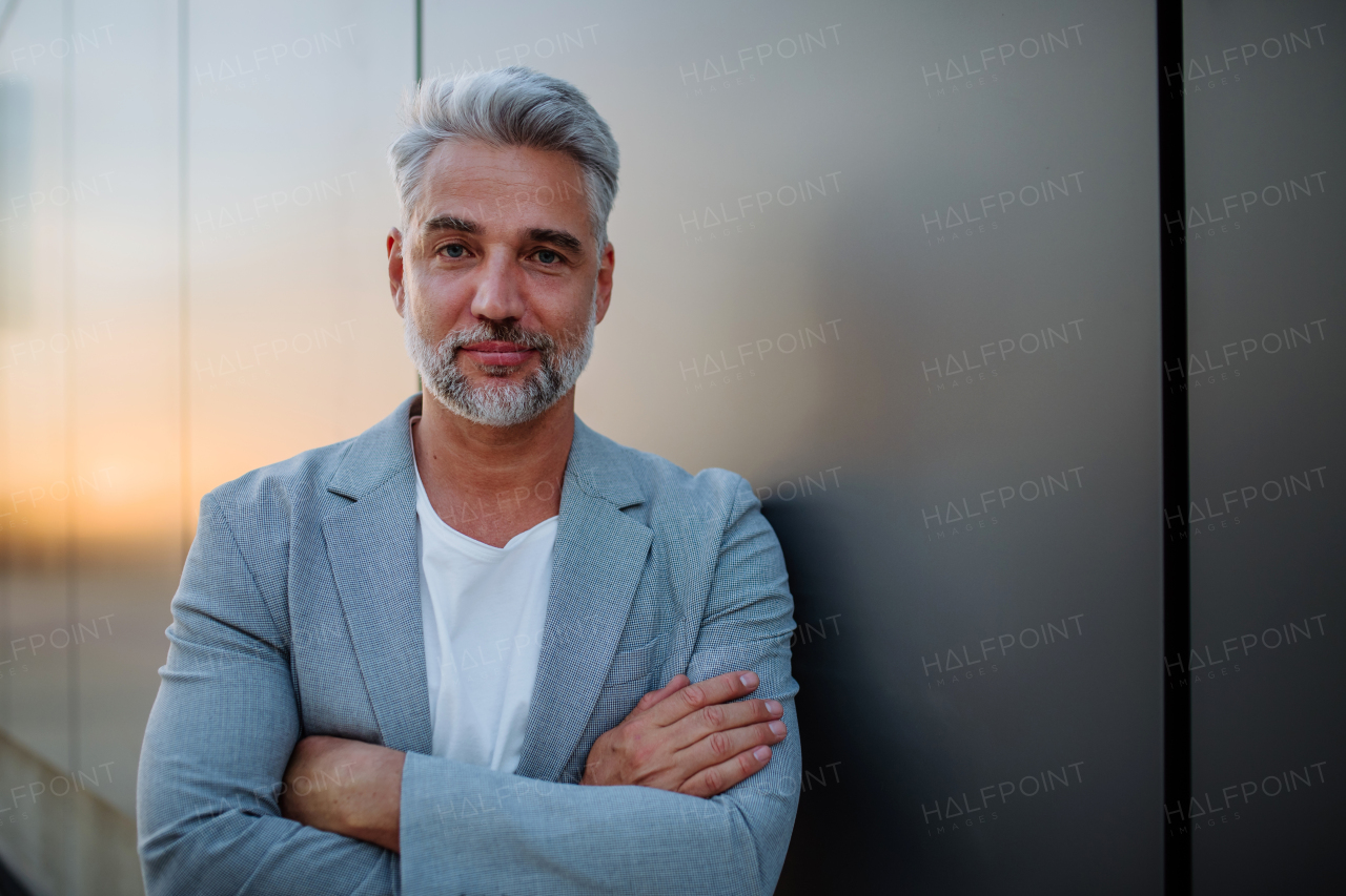 A mature relaxed businessman leaning on street wall, work life balance concept.