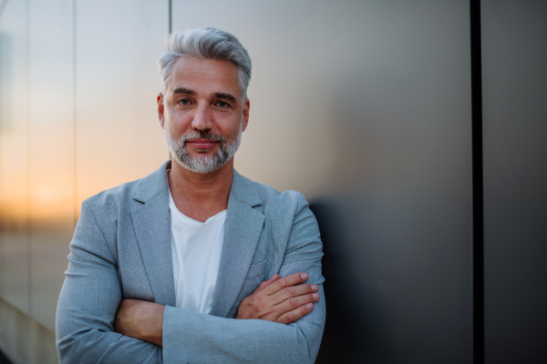 A mature relaxed businessman leaning on street wall, work life balance concept.