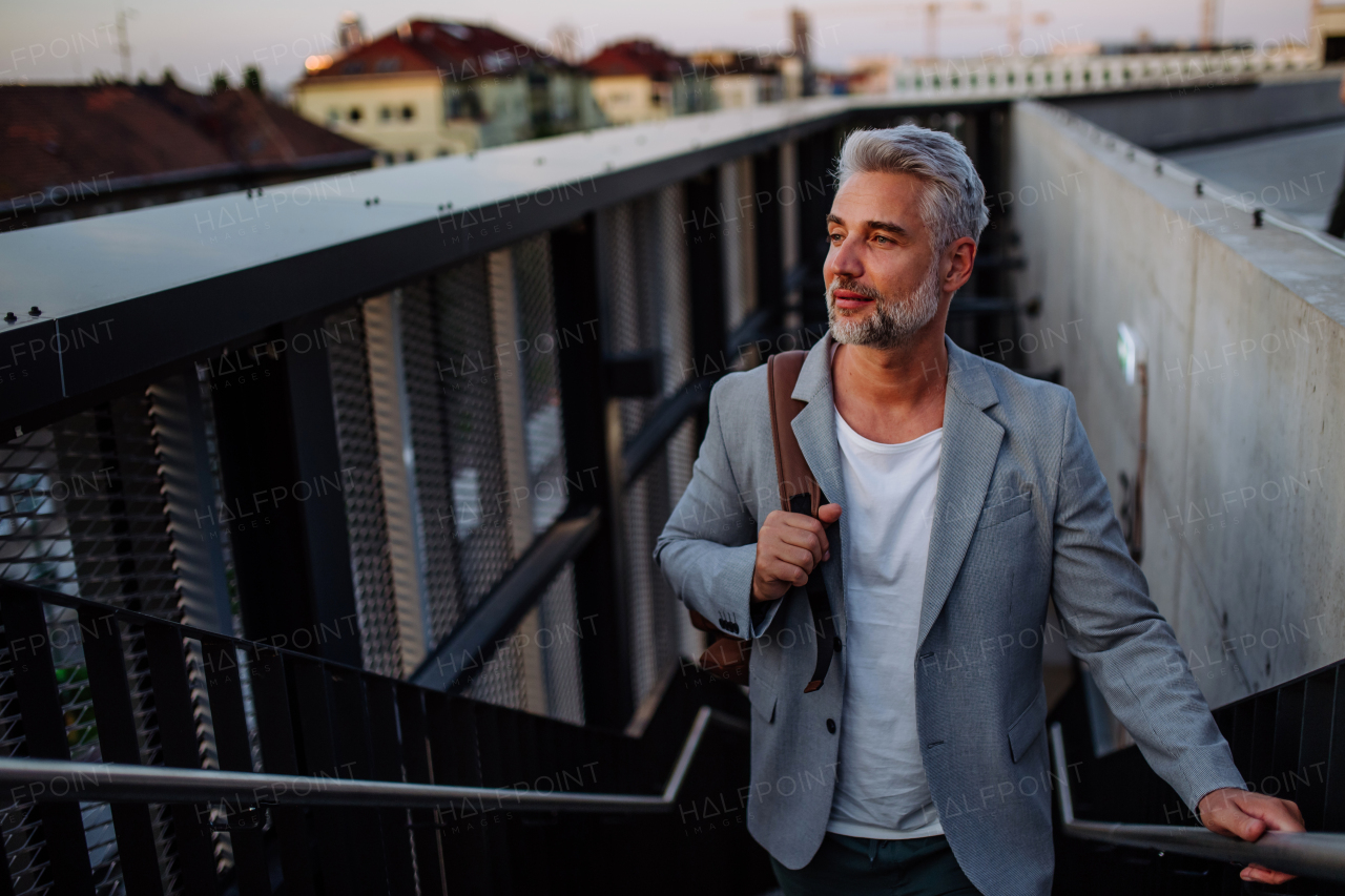 A successful happy businessman commuting in city staircase, looking away.