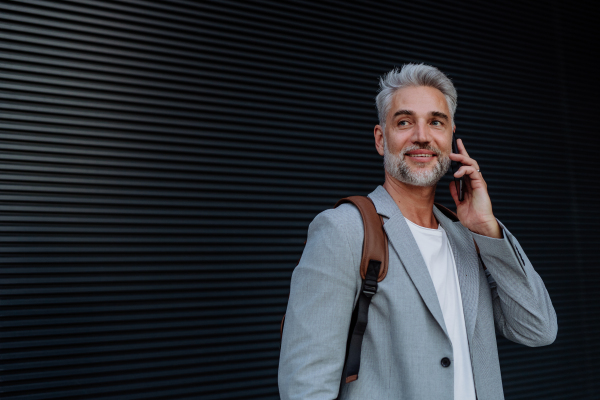 A successful happy businessman waiting in city street, calling on mobile phone, commuting concept.