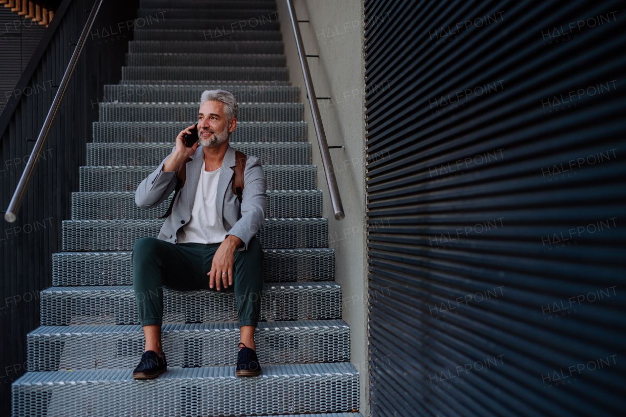 A successful happy businessman waiting in city street, calling on mobile phone, commuting concept.