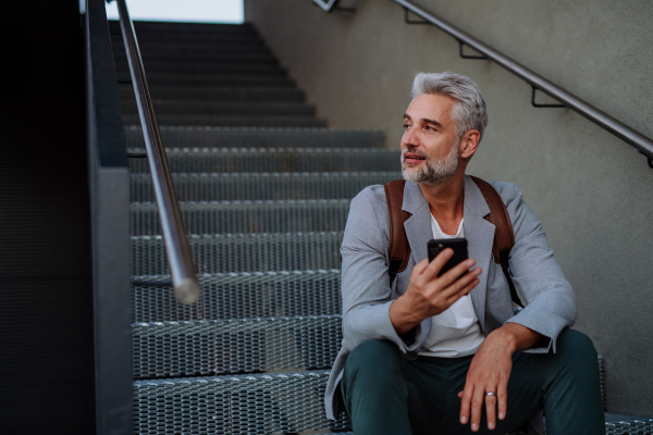 A successful happy businessman waiting in city street, calling on mobile phone, commuting concept.