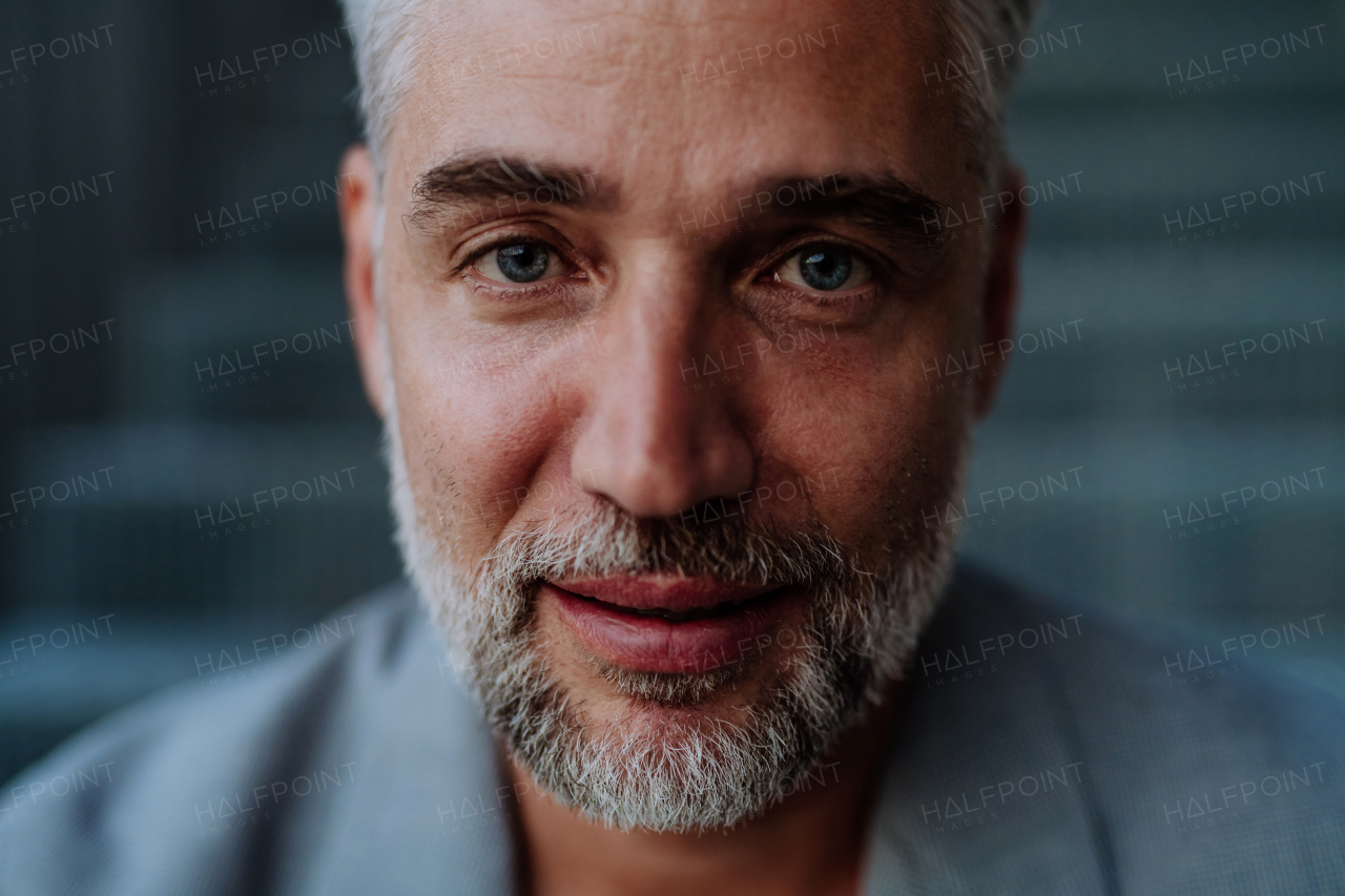 Close-up portrait of handsome mature businessman sitting out, looking at camera.