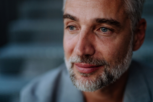 Close-up portrait of handsome mature businessman sitting out, looking at camera.