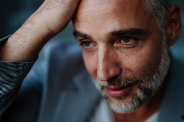 A close-up portrait of handsome businessman touching his head looking away and thinking or making some decision