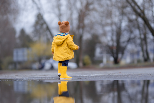 Happy little boy jumping in puddle after rain in cold autumn day.