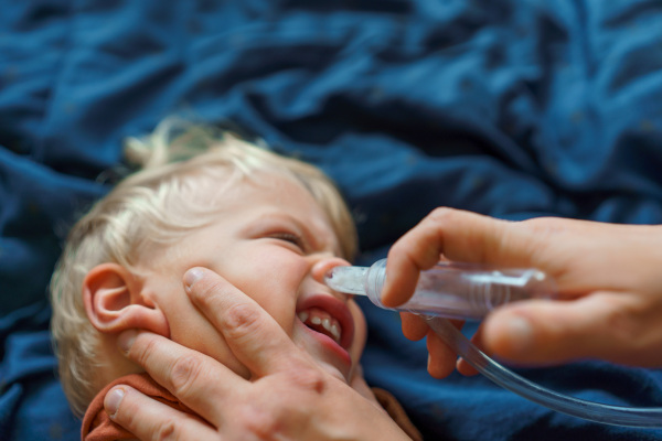 Close-up of parent holding his kid and using snot extractor.