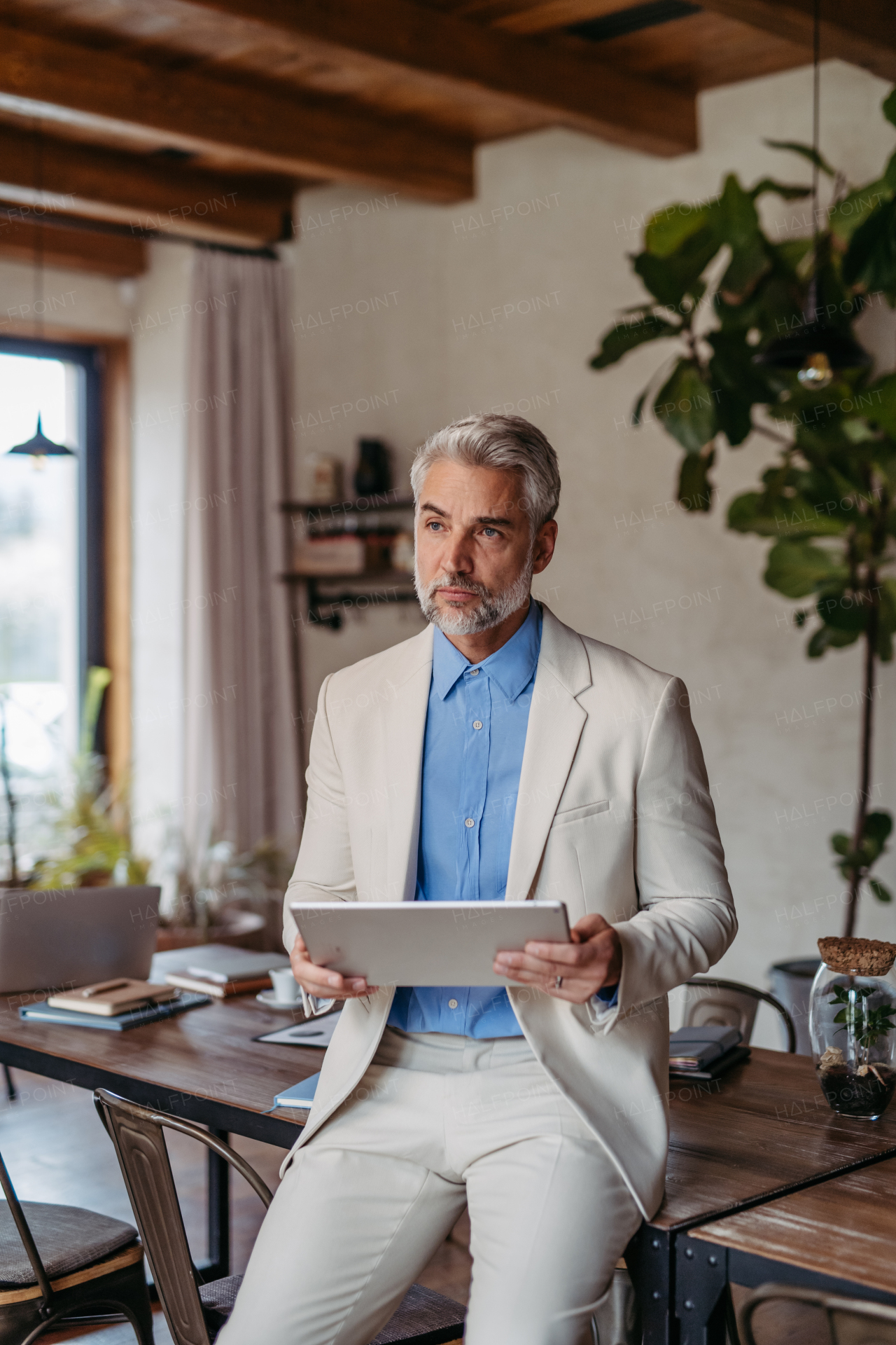 Portrait of handsome businessman leaning against a desk in a modern office. Male corporate leader, executive, manager using digital tablet.