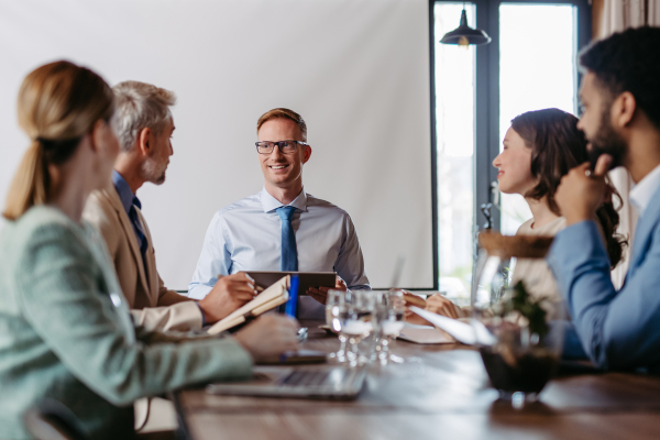 Young colleagues having casual discussion during business meeting in office. Group of men and women sitting in conference room.