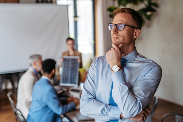 Portrait of confident young businessman during team meeting. Young colleagues discussing photovoltaic panels, clean, green, energy. Business using renewable energy.