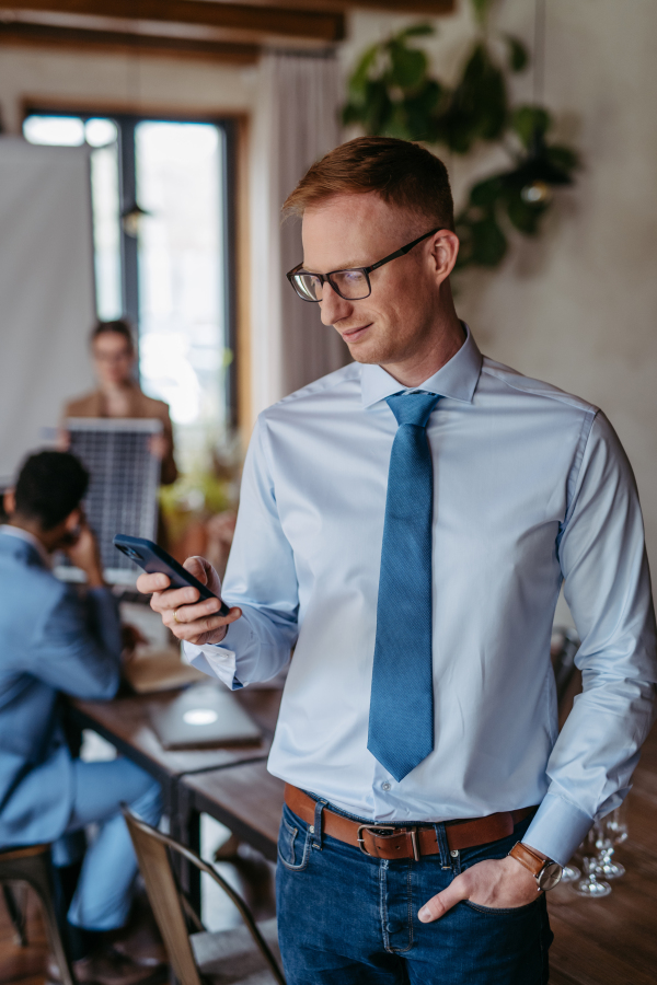 Portrait of confident young businessman using smart phone during meeting. Group of men and women sitting in conference room.