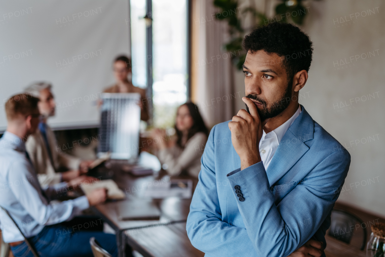 Portrait of confident young businessman during team meeting. Group of men and women sitting in conference room.