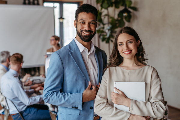 Portrait of confident young colleagues during team meeting. Businesswoman and businessman in the office in font of their team.